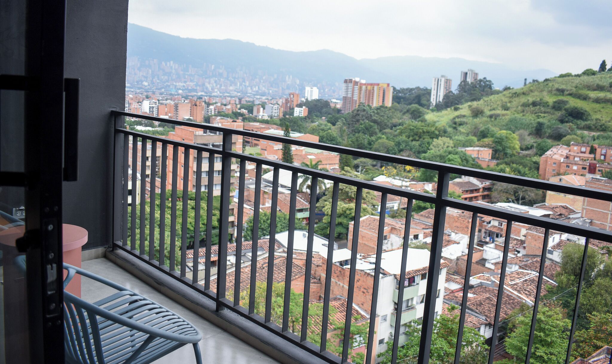 Balcón con barandilla metálica que ofrece vistas a un paisaje urbano con edificios y zonas verdes.