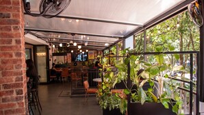Un café intérieur aux murs de briques, avec des tables, des chaises et des plantes suspendues.
