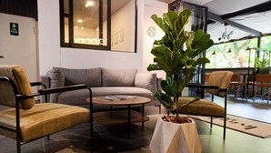 A modern interior with a sofa, two armchairs, a coffee table, and a large potted plant. - Hotel Living 35 Suites by Growing Group (Medellín)
