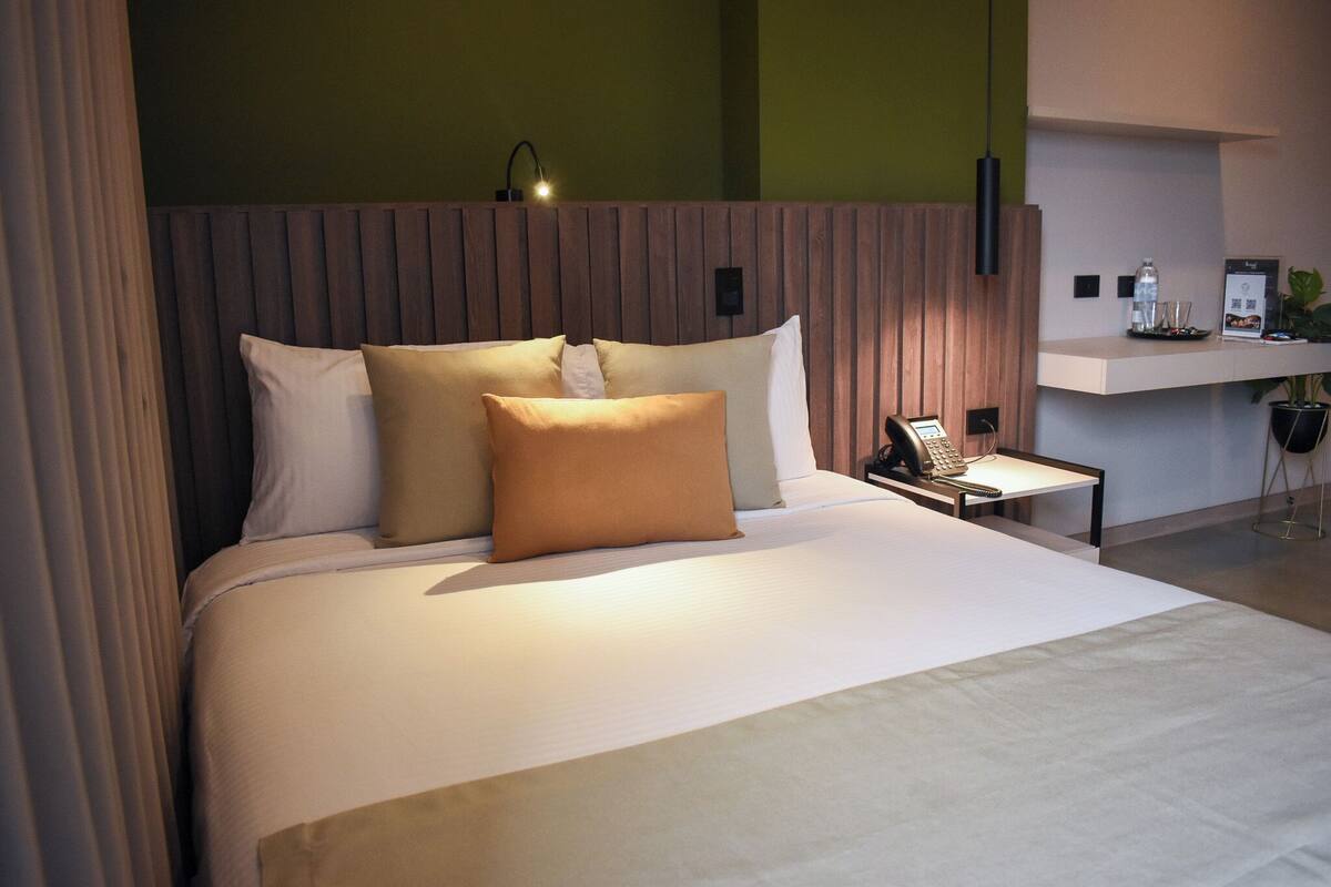 Een moderne hotelkamer met een groot bed, een nachtkastje met telefoon en lamp, en een klein bureau met computer.