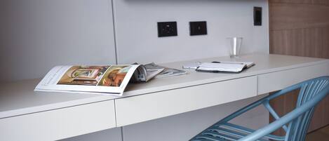 A modern office desk with a magazine, a notebook, and a pen. A blue chair is positioned in front of the desk.