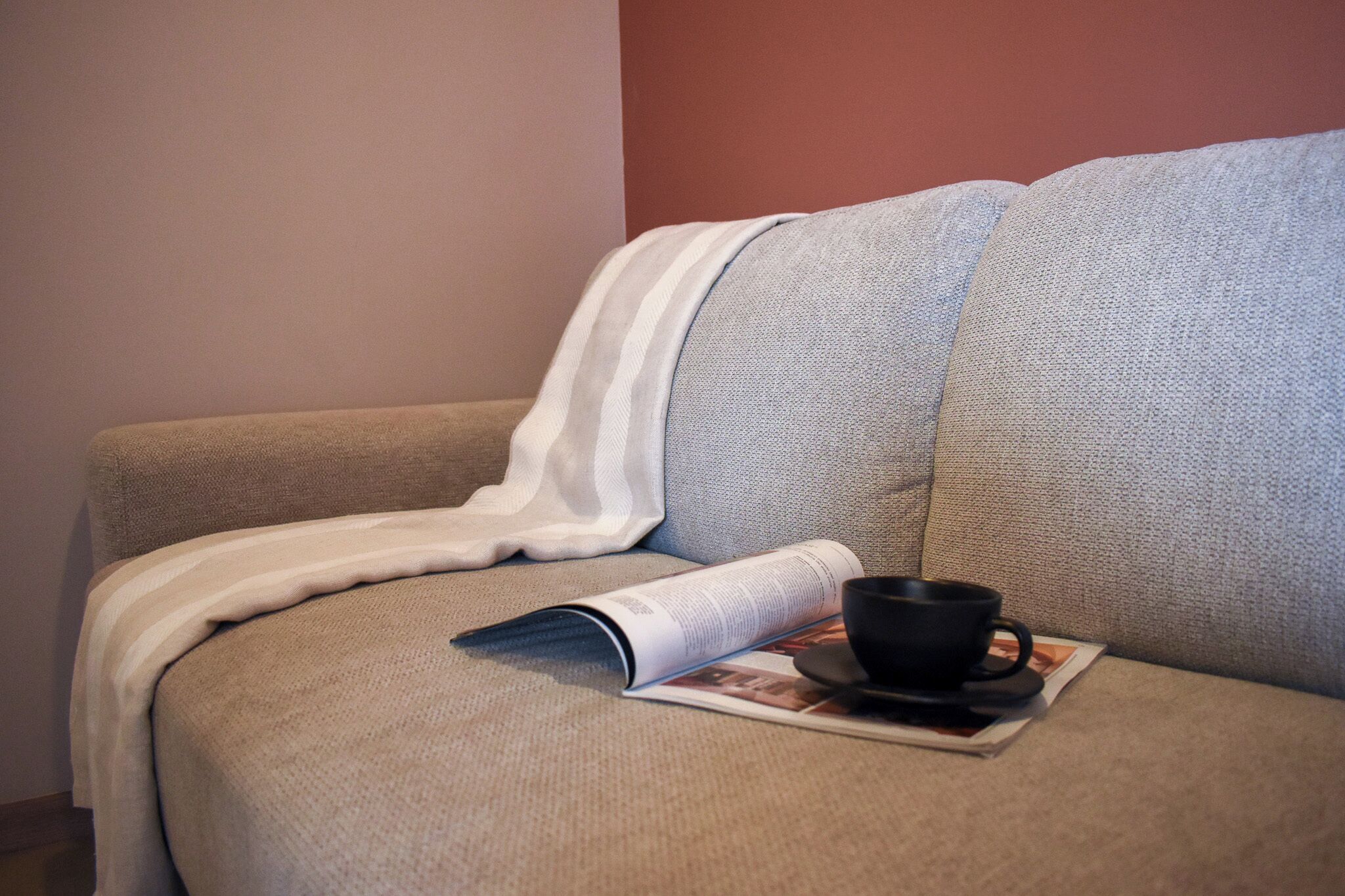 A sofa with a magazine and a cup.