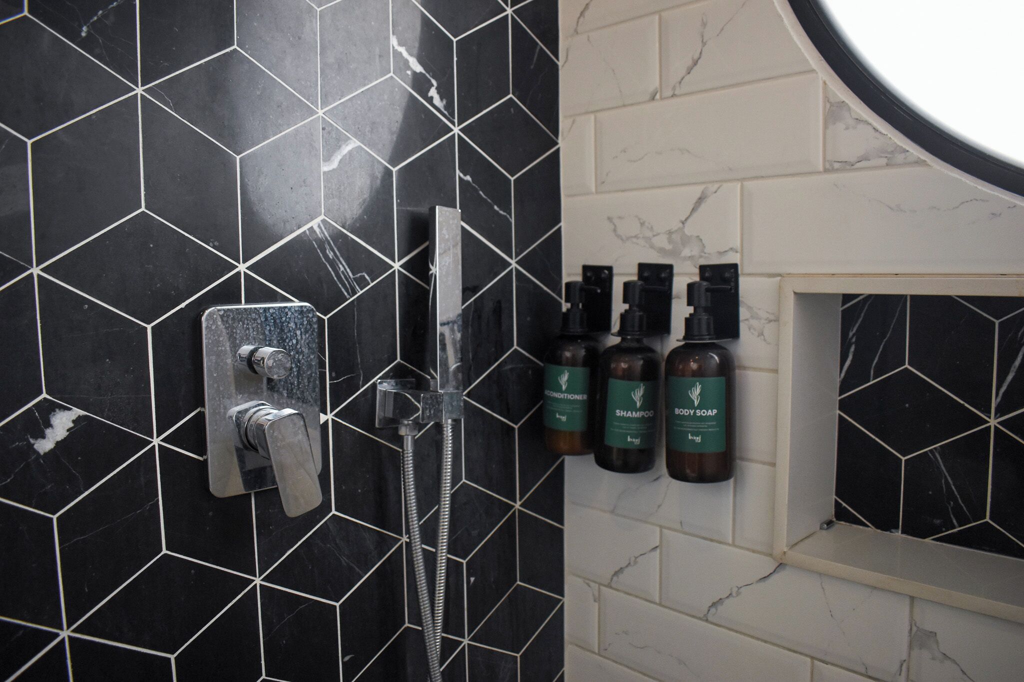 A bathroom with black hexagonal tiles, a silver showerhead, and two bottles of body soap.