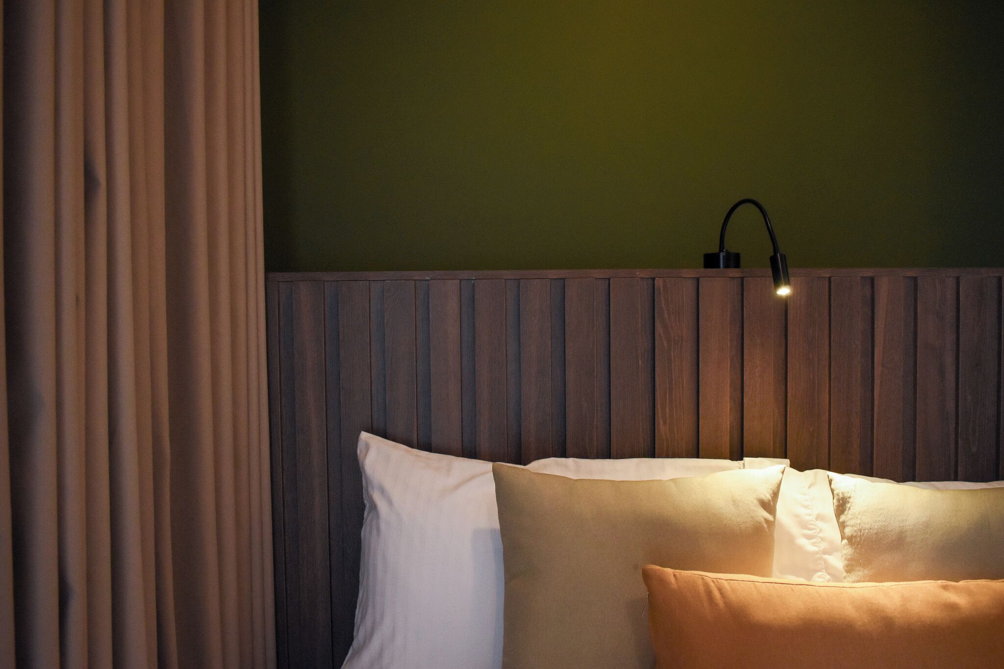 A bed with white and beige pillows, a wooden headboard, and a wall-mounted light fixture.