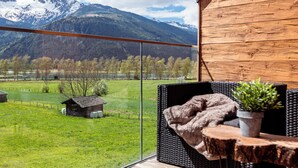 Un balcón con vistas a una cadena montañosa, una cabaña de madera y un cobertizo pequeño en un campo verde.