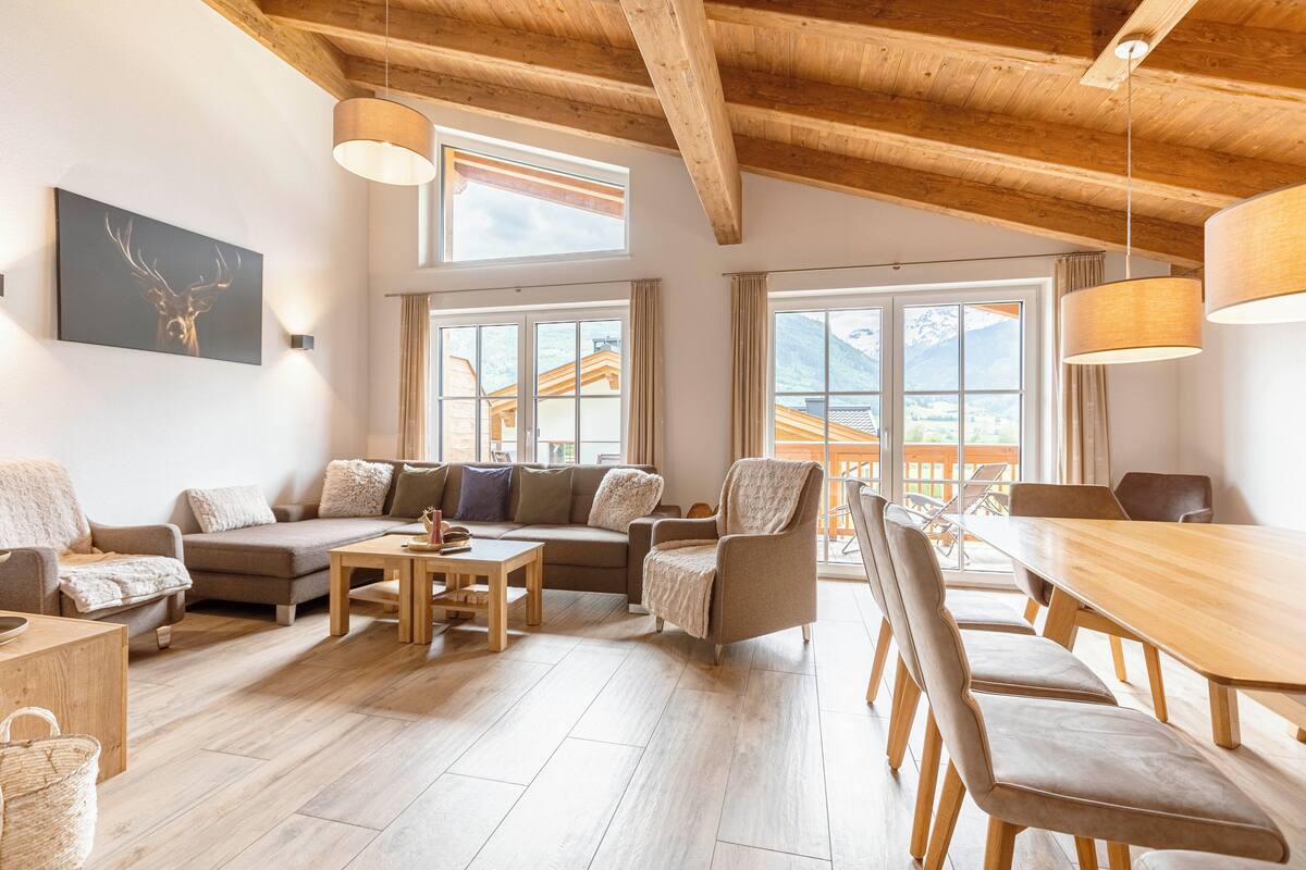 Amplia sala de estar con techo de madera, ventanas grandes, un conjunto de sofás, una mesa de comedor y sillas.