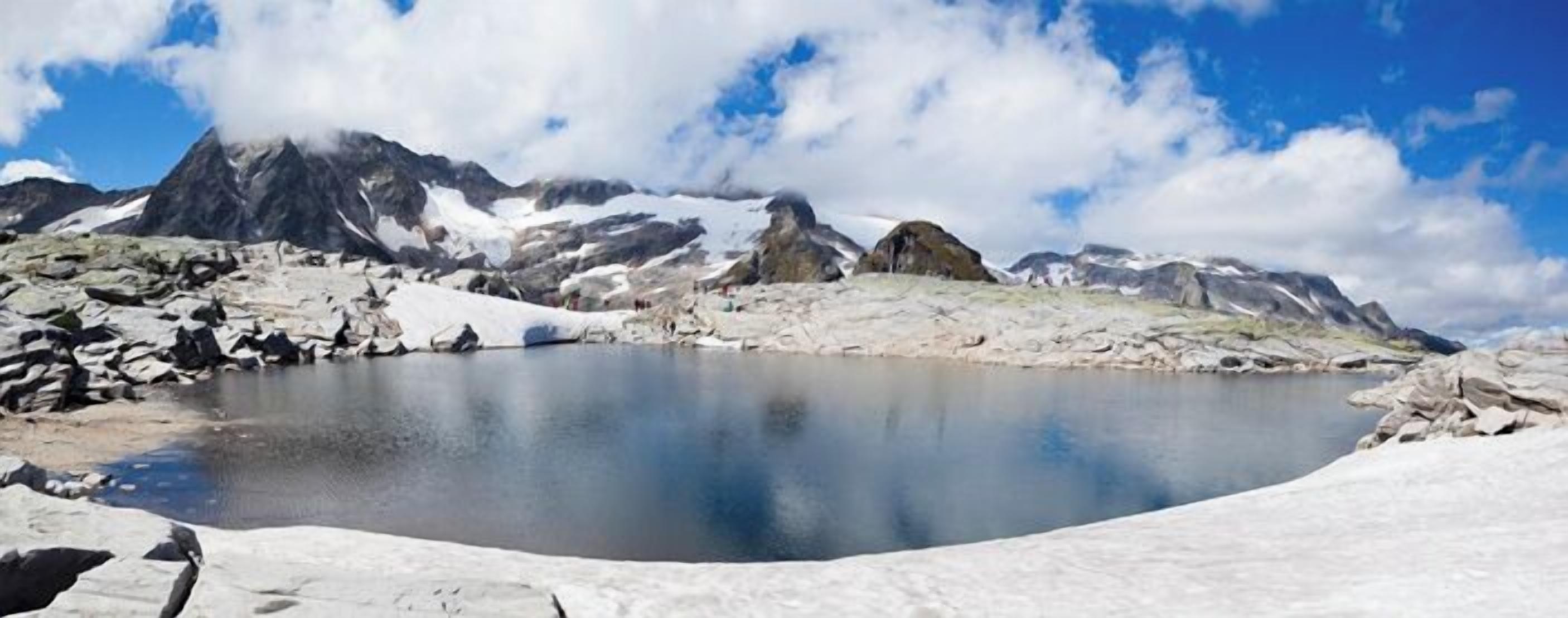 Un lago montano tranquillo con sponde rocciose e cime innevate sullo sfondo.