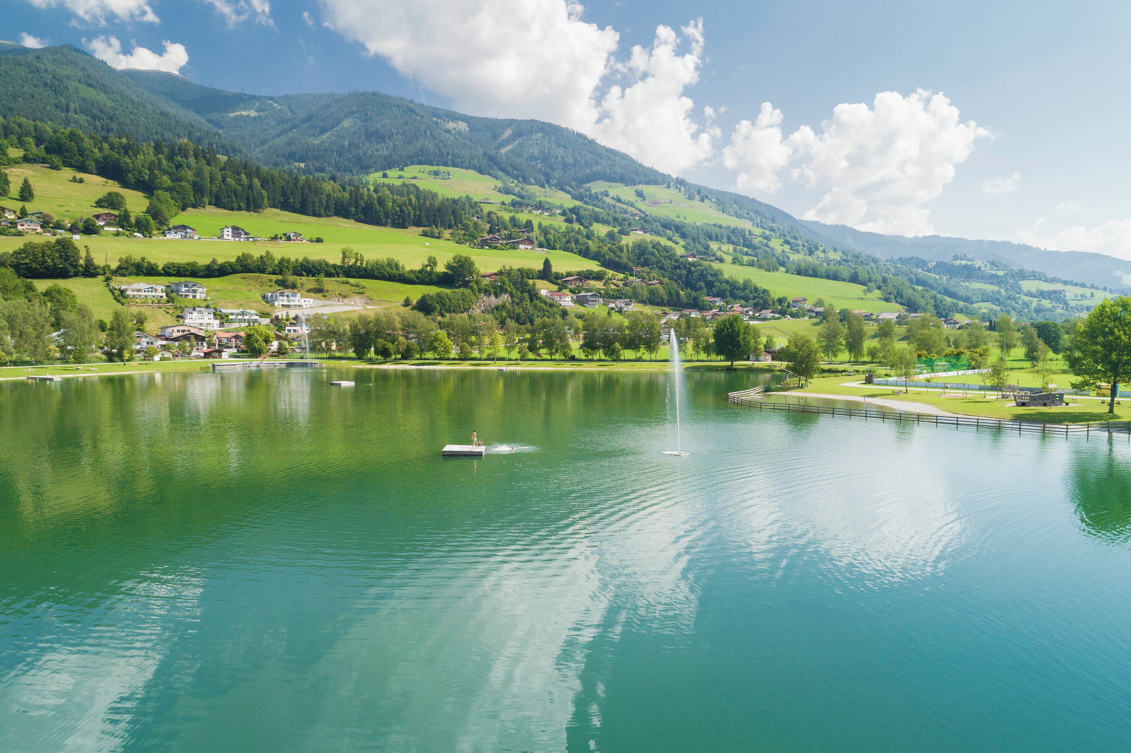 Un lago con una fuente, rodeado de colinas verdes y casas.
