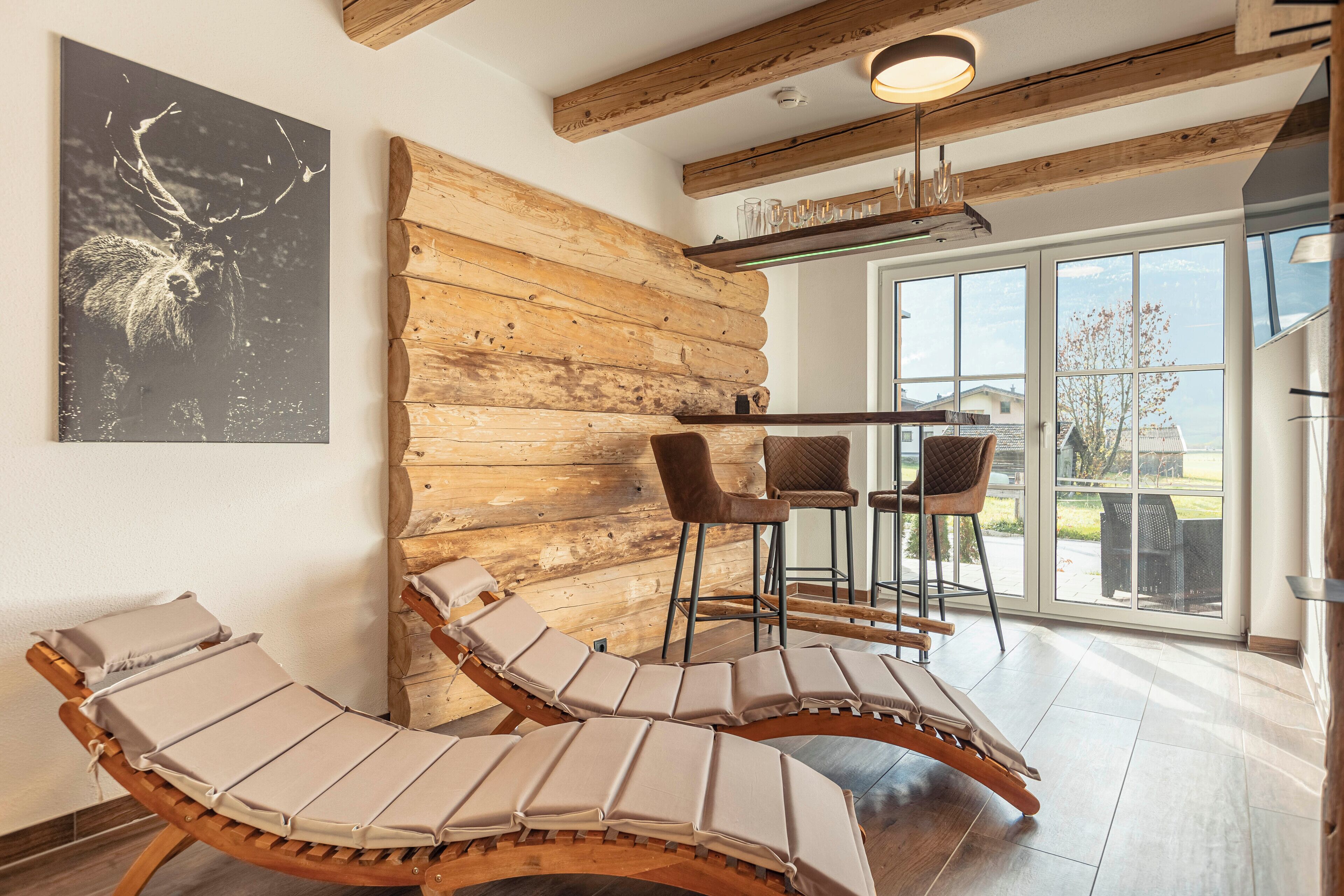L’intérieur d’une cabane en rondins, avec un mur en bois, un coin repas avec des chaises et une grande fenêtre donnant sur un paysage.