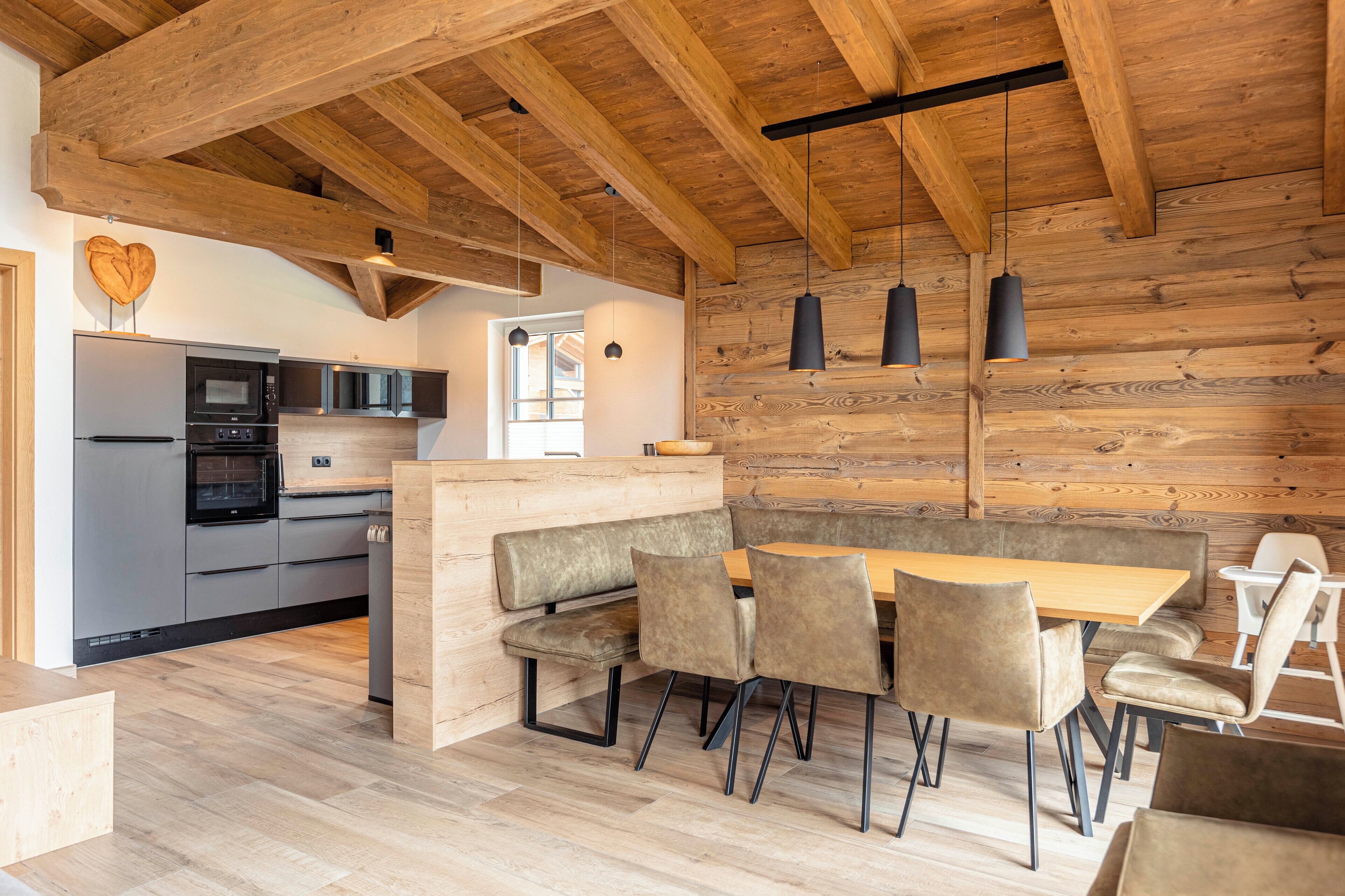 Eine moderne Küche mit Holzbalken, einem Einbauofen und einer Essecke mit einer Bank und Stühlen.