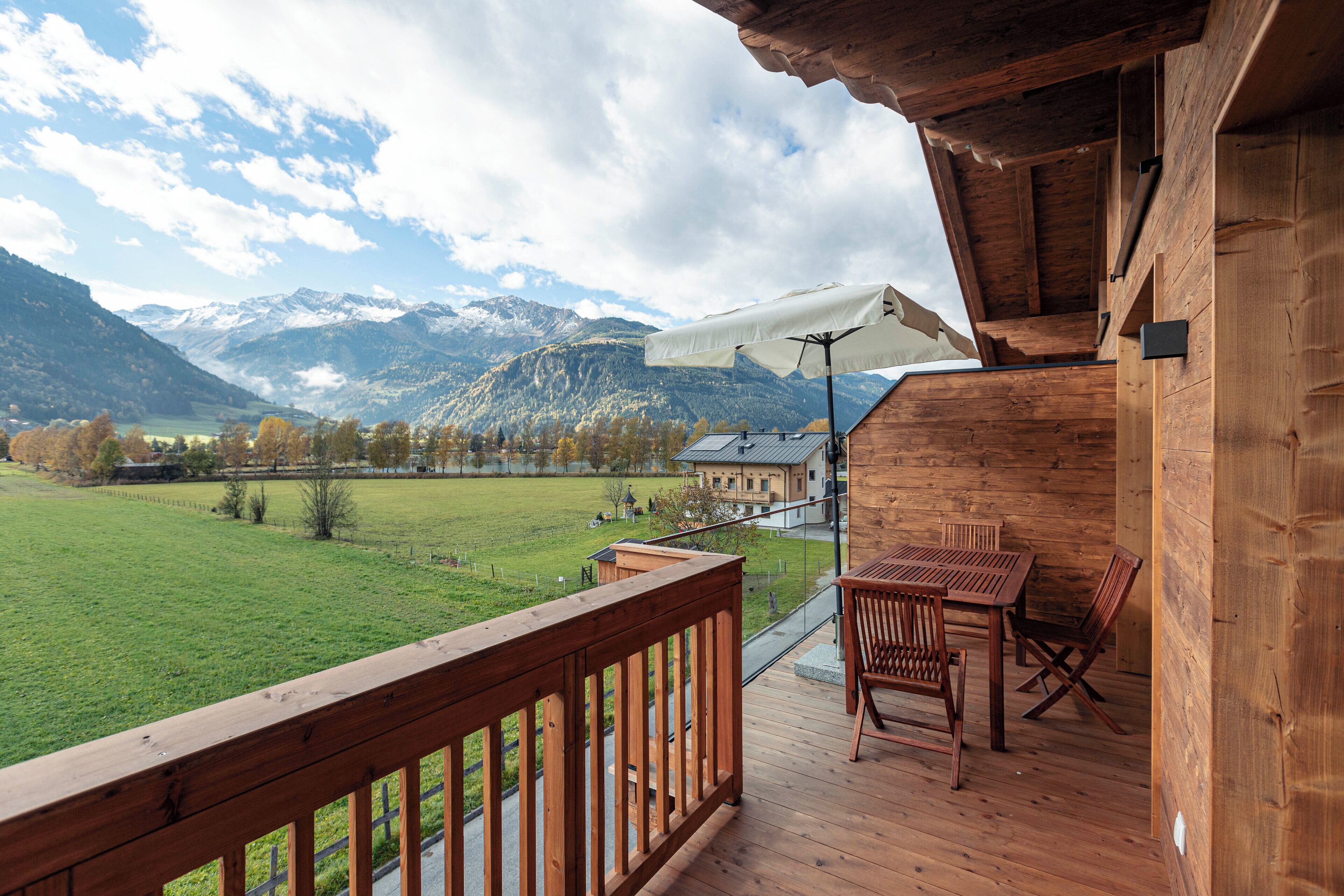 Una terraza de madera con una mesa y sillas, con vistas a un campo verde y montañas.