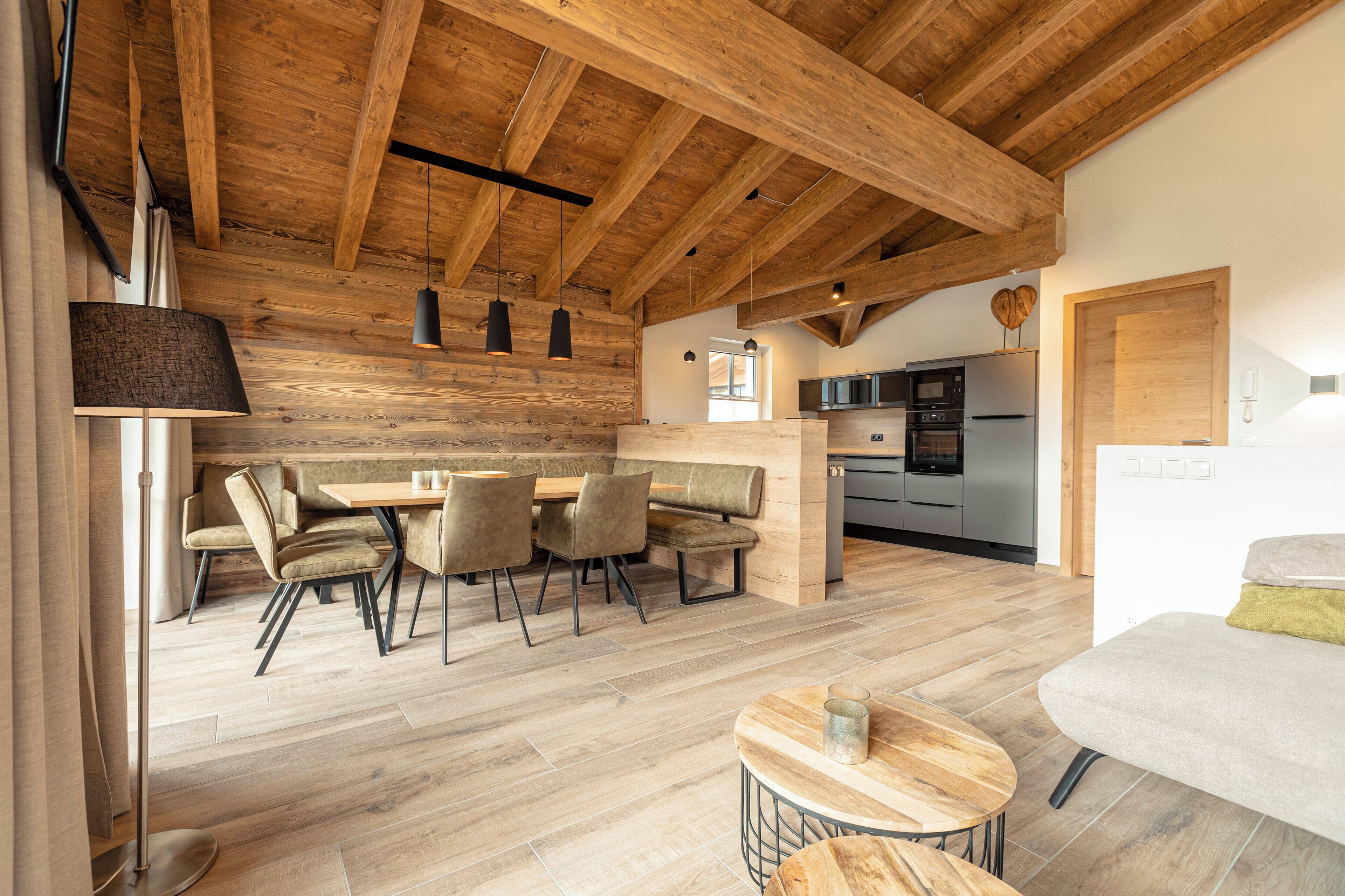 Una cocina moderna con horno empotrado y microondas, vigas de techo de madera, y un comedor con mesa y sillas.
