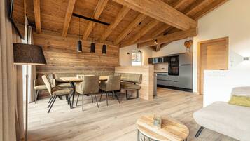 Una cocina moderna con horno empotrado y microondas, vigas de techo de madera, y un comedor con mesa y sillas.
