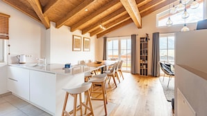 Una cocina moderna con vigas de madera, un comedor con taburetes y un amplio ventanal con cortinas.
