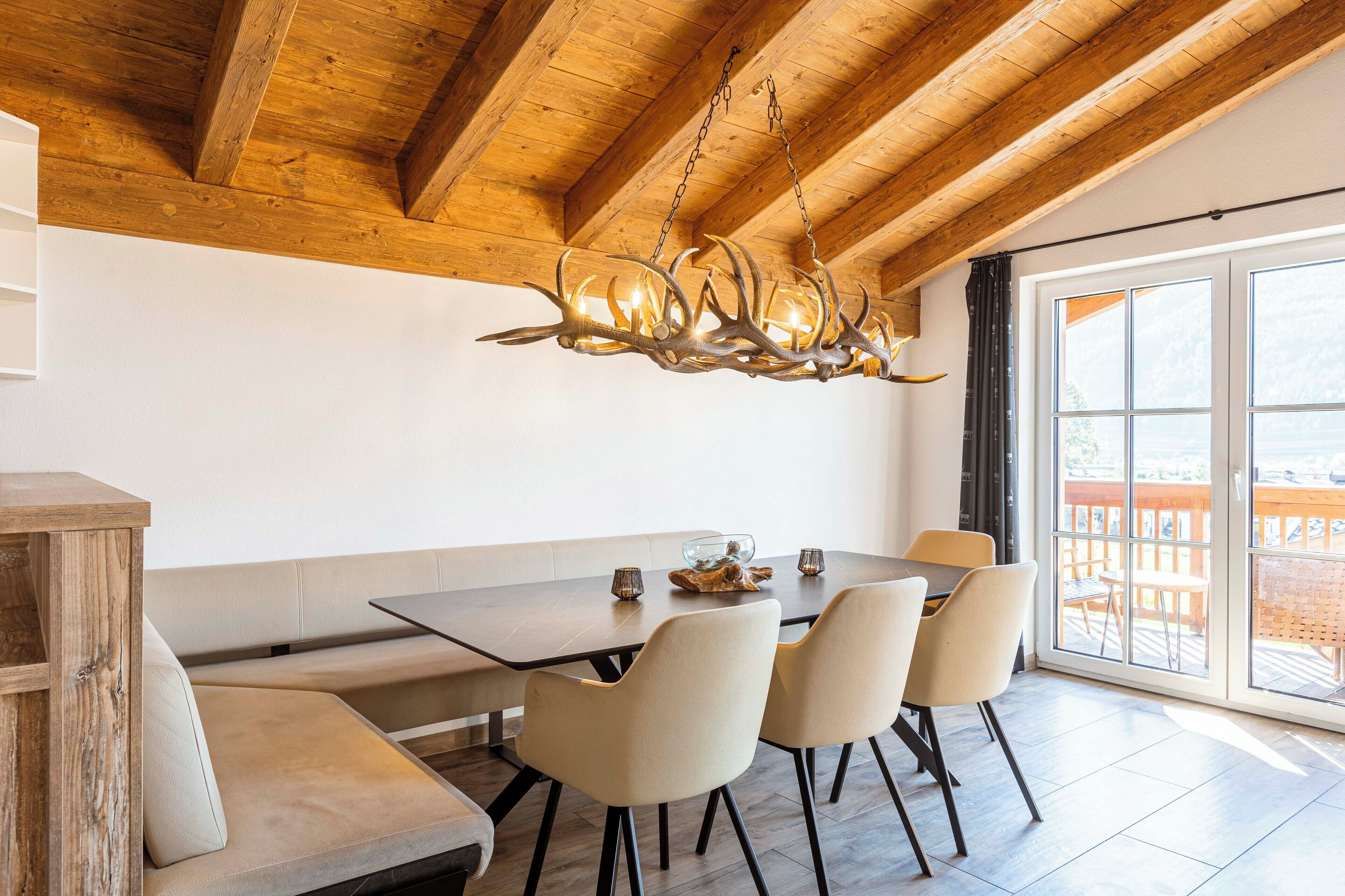 A dining area with a wooden ceiling, a chandelier, a large window, and a view of the outdoors.