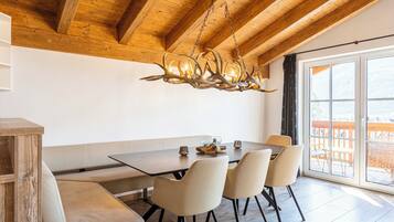 A dining area with a wooden ceiling, a chandelier, a large window, and a view of the outdoors.