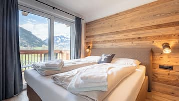 Ein Schlafzimmer mit zwei Betten, einem Holz-Kopfteil und Blick auf Berge durch große Fenster.