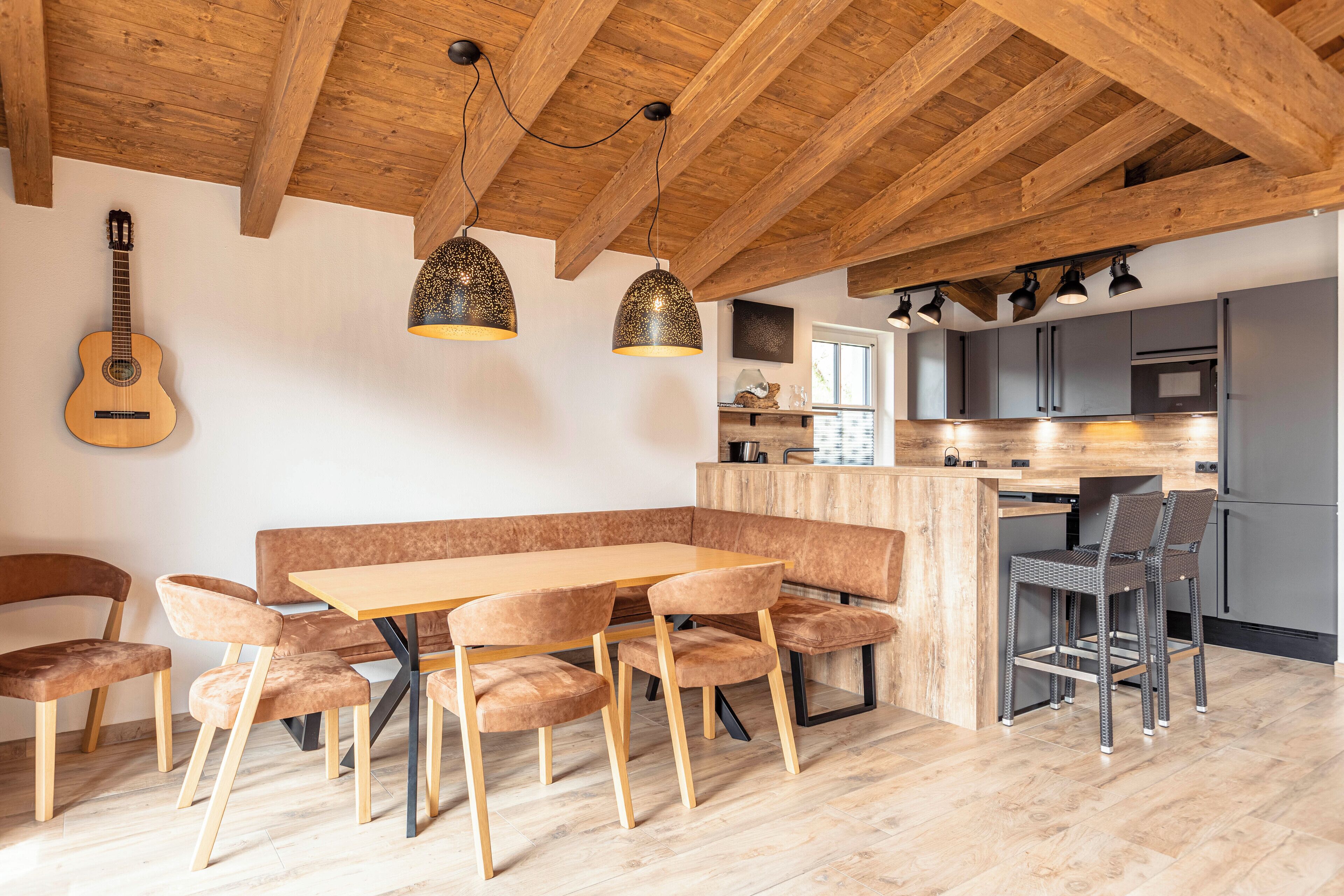 Una cocina moderna con techo de madera, un área de comedor con mesa de madera y sillas acolchadas, y una isla de cocina con taburetes de bar.