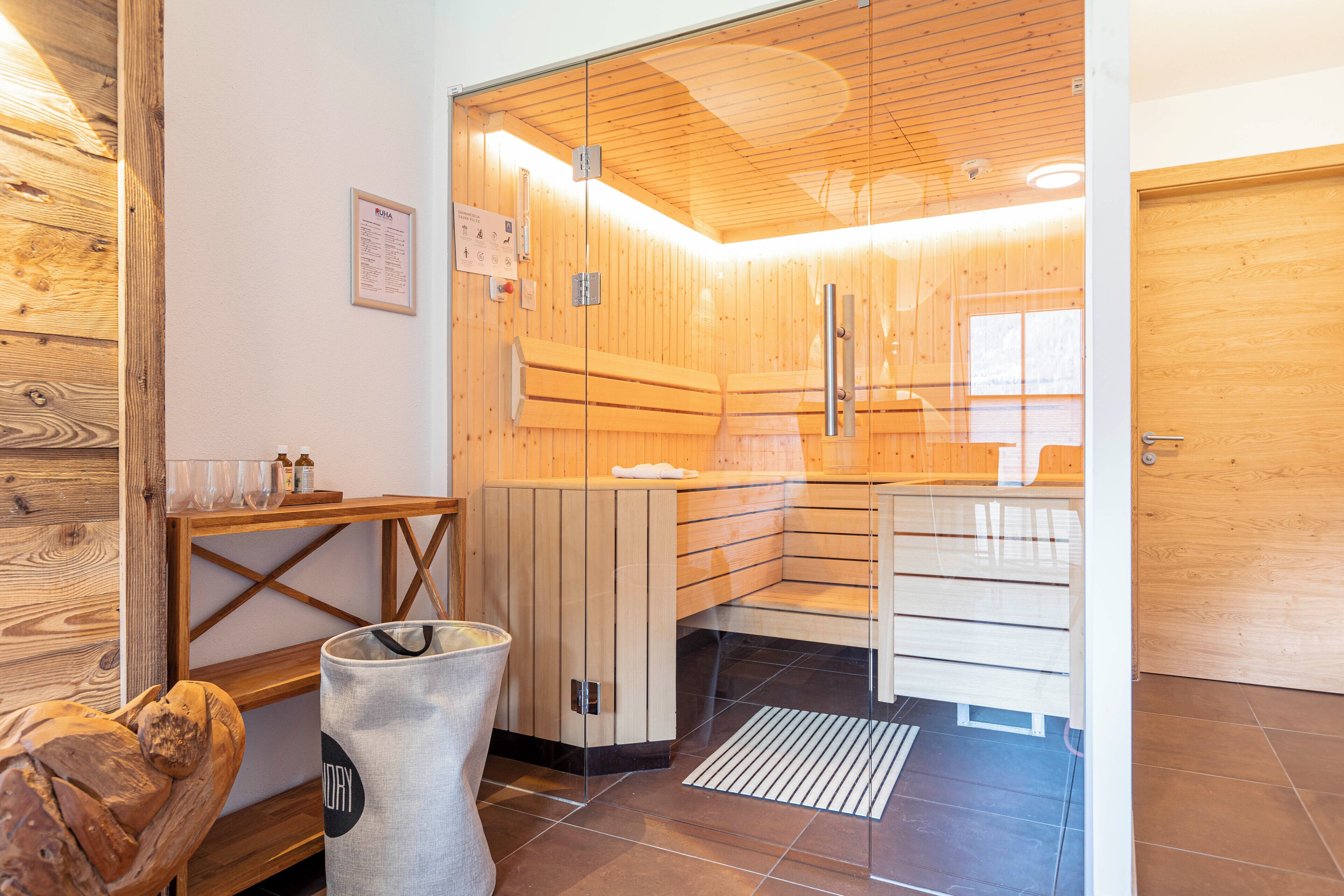 A sauna room with wooden walls and benches, a glass door, and a wooden door.