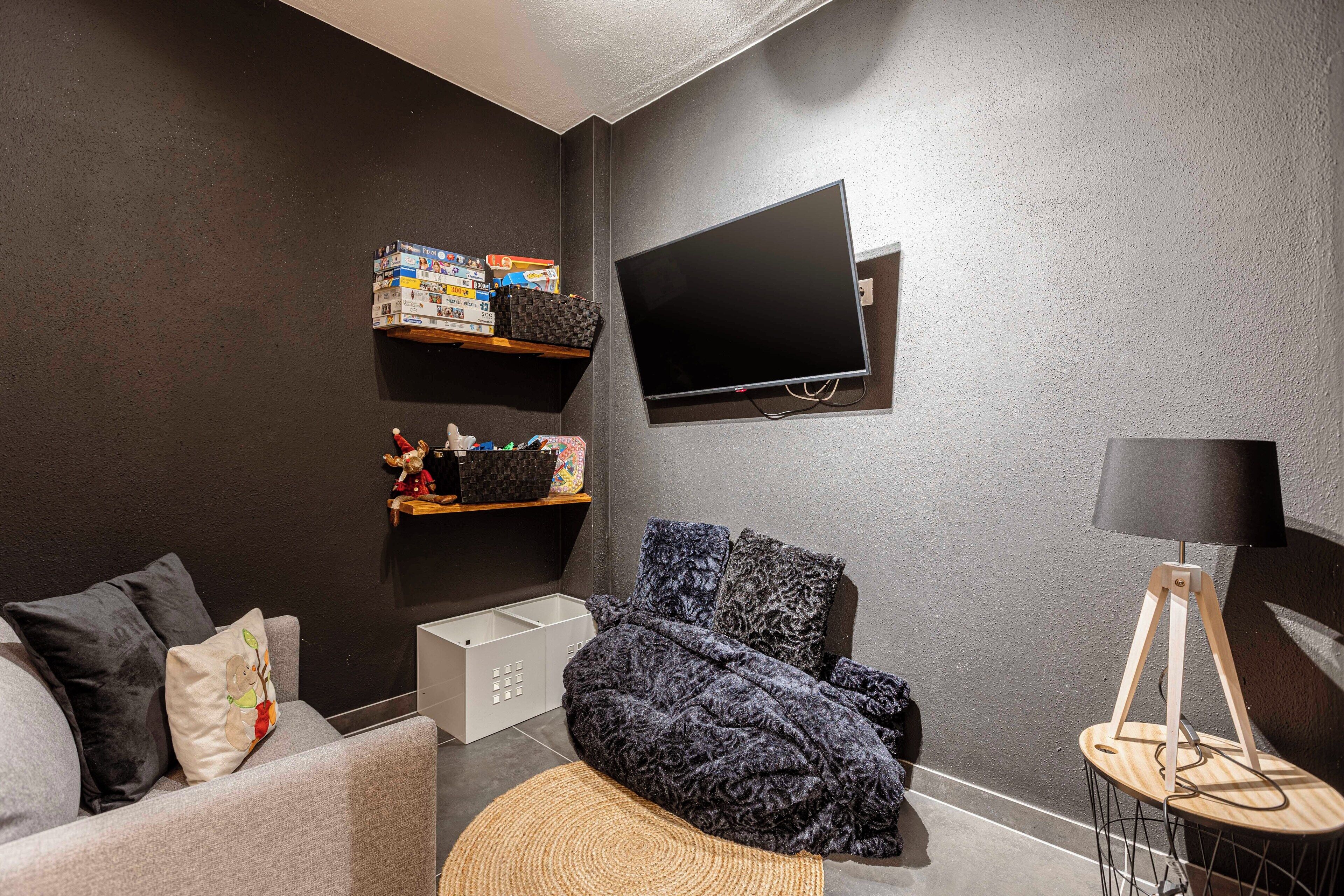 Ein gemütliches Wohnzimmer mit grauem Sofa, einem gemusterten Überwurf, einem Flachbildfernseher und einer Lampe.