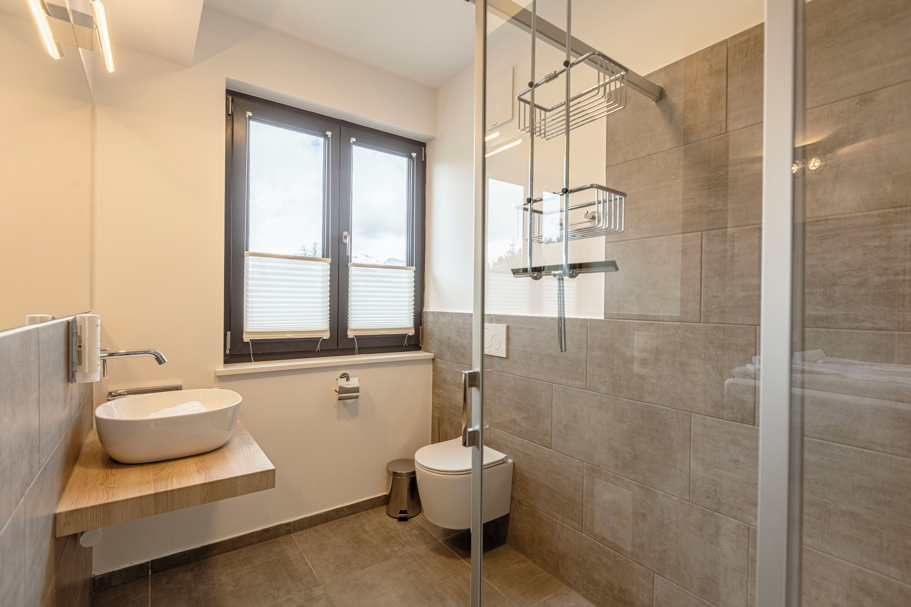 A modern bathroom with a large window, a vessel sink, a toilet, and a glass shower enclosure.