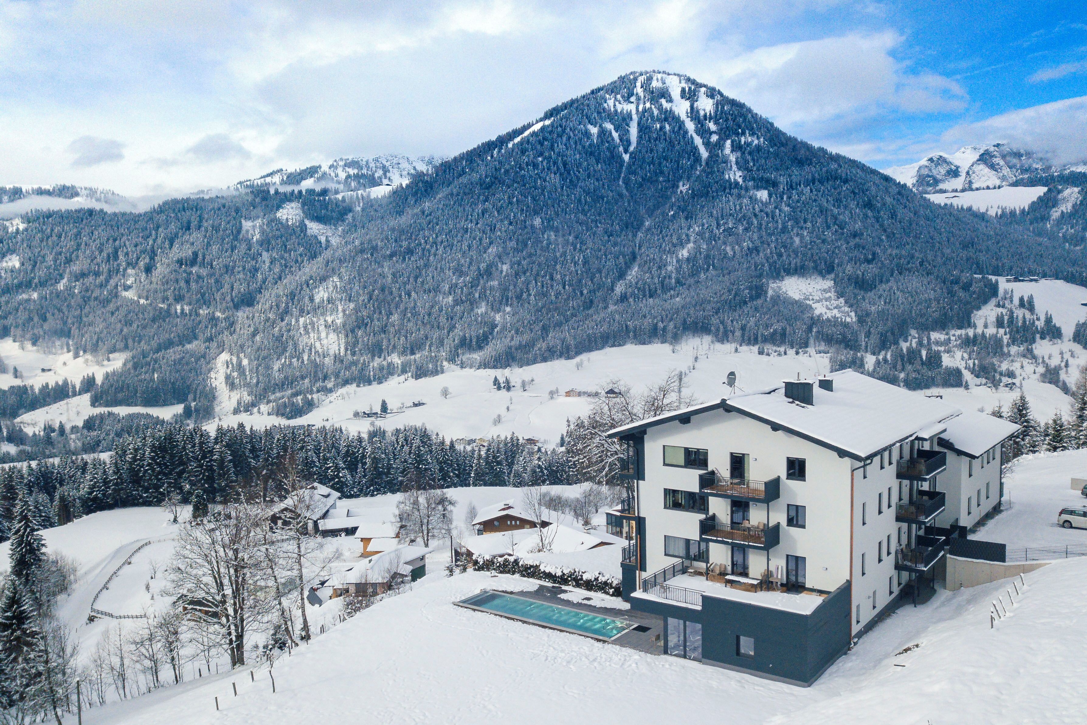 Un hôtel moderne doté d’une piscine, entouré de montagnes et d’arbres couverts de neige.