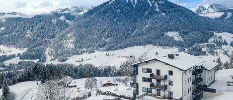 Un hôtel moderne doté d’une piscine, entouré de montagnes et d’arbres couverts de neige.