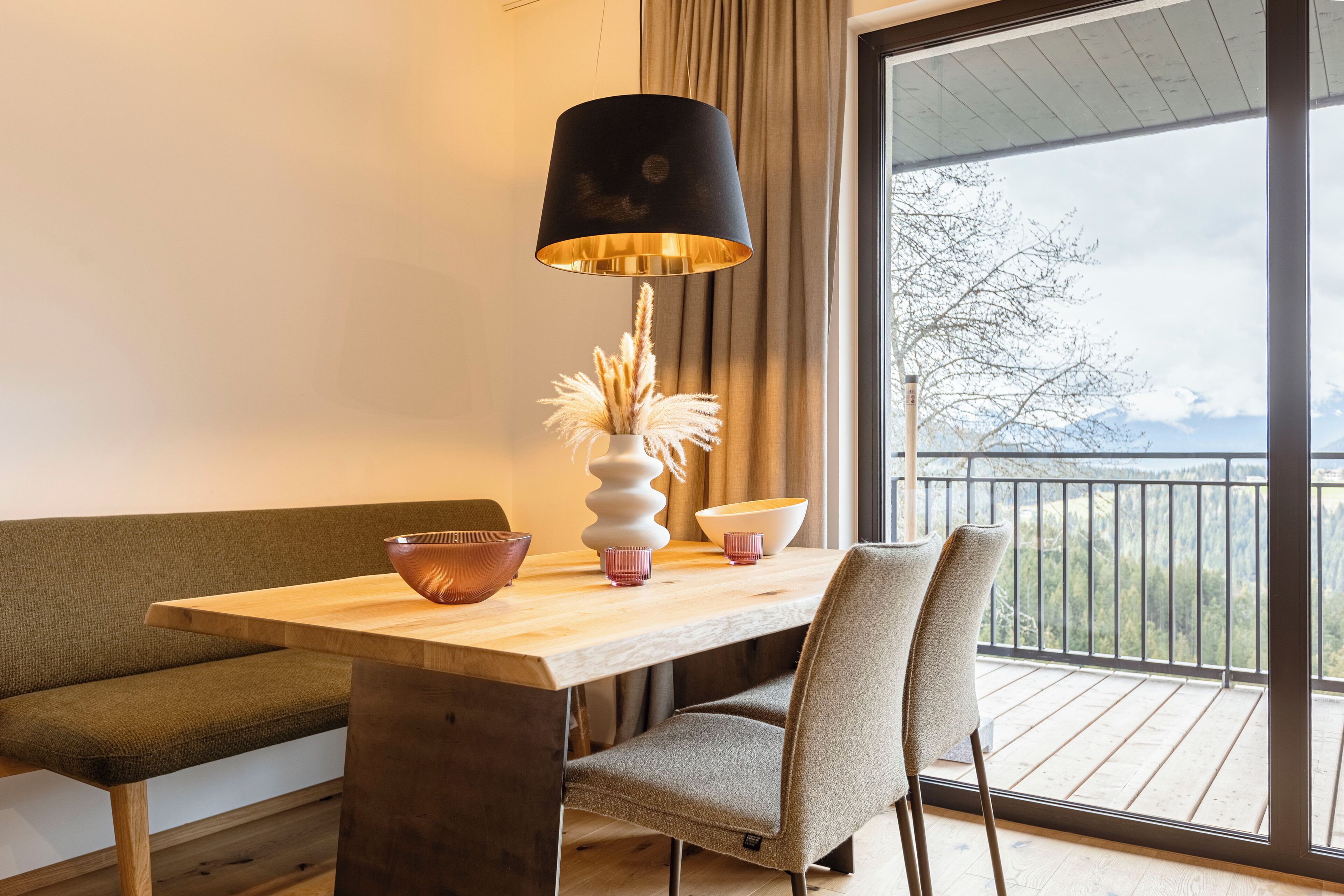 Un comedor moderno con una mesa de madera, sillas, una lámpara y vistas a un balcón con barandilla.