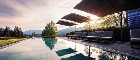 A pool with lounge chairs and umbrellas, surrounded by trees and mountains.
