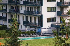 Un hotel de varios pisos con balcones, piscina y sillones de descanso.
