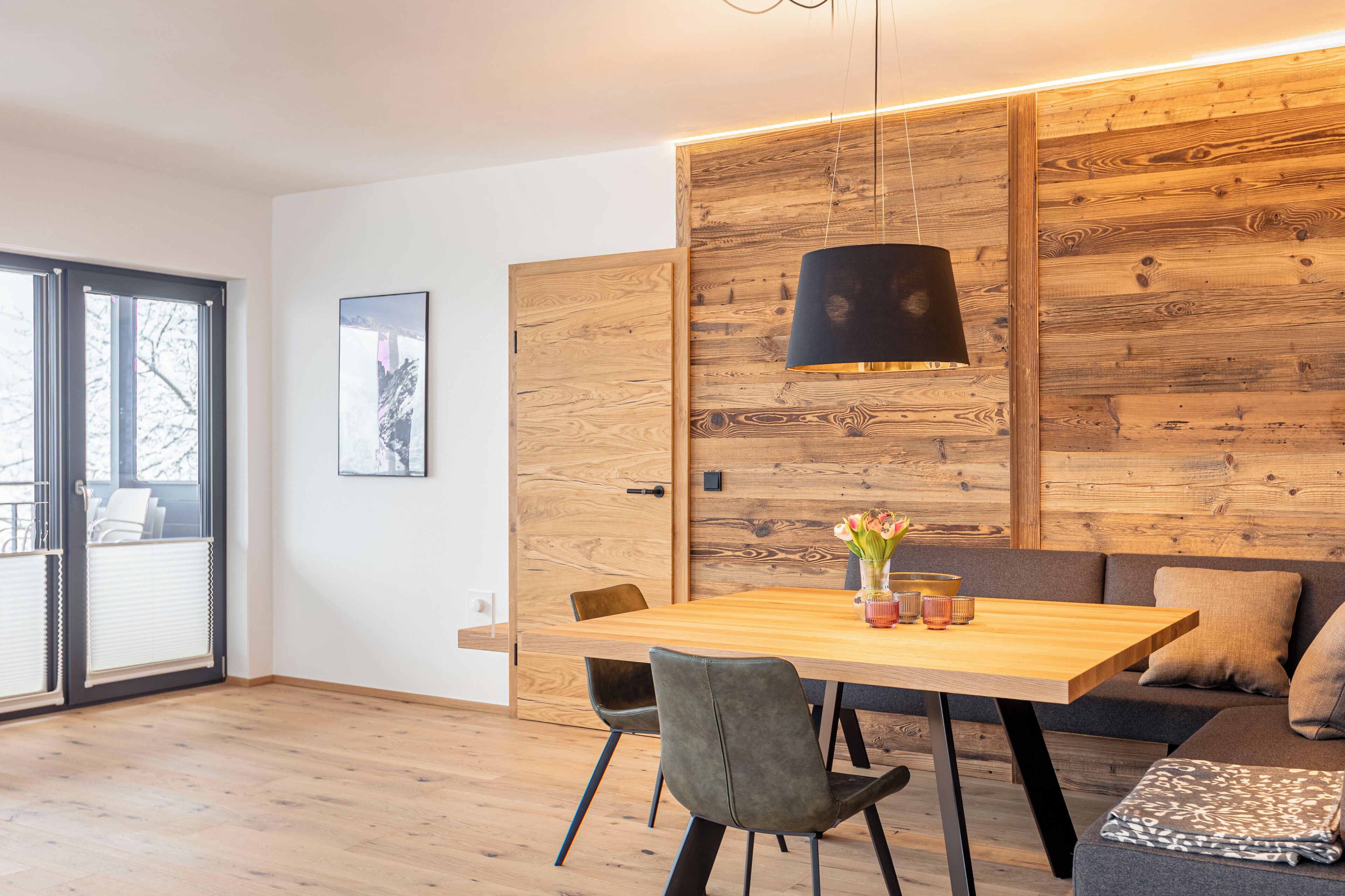 A modern dining area with a wooden table, chairs, and a hanging light fixture.