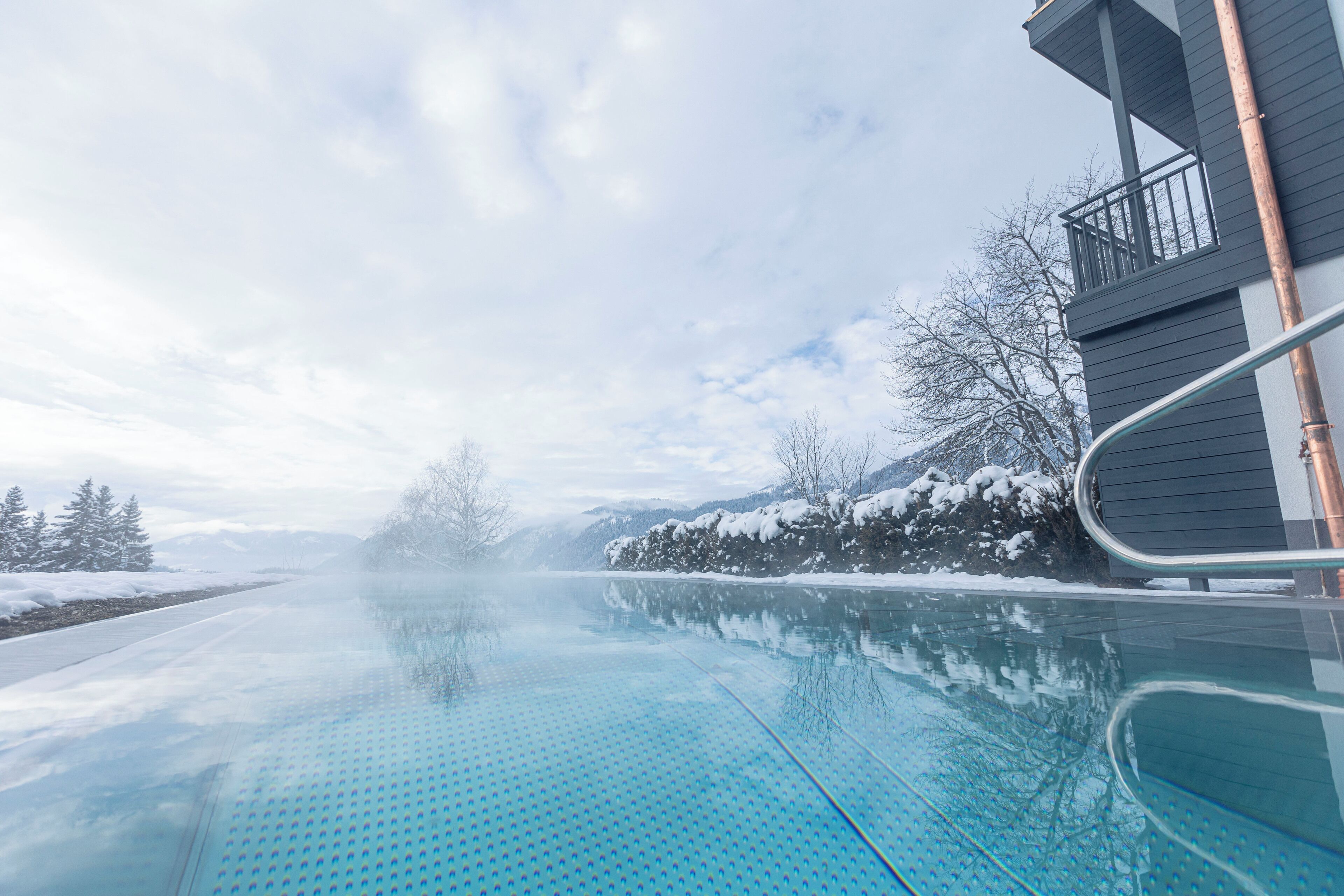 Piscina con vista despejada a una casa y un paisaje nevado al fondo.