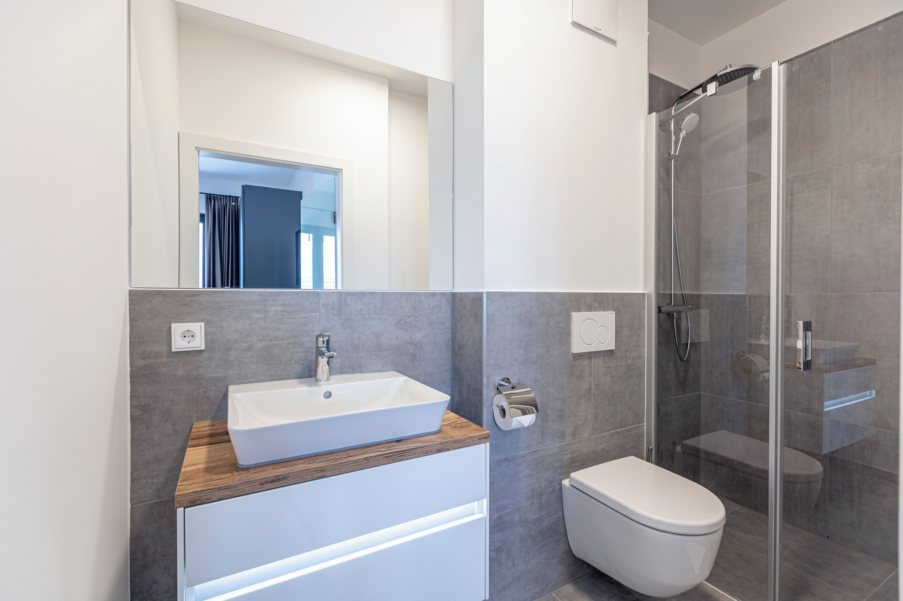Un baño moderno con un lavabo blanco, encimera de madera y cabina de ducha con mampara de vidrio.