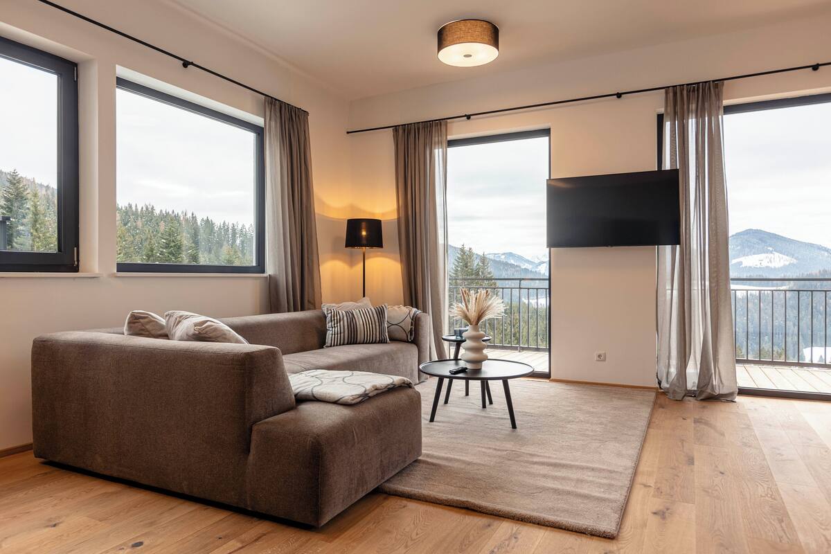 Ein modernes Wohnzimmer mit einer Couch, einem kleinen Tisch mit Lampe und einem an der Wand befestigten Fernseher.
