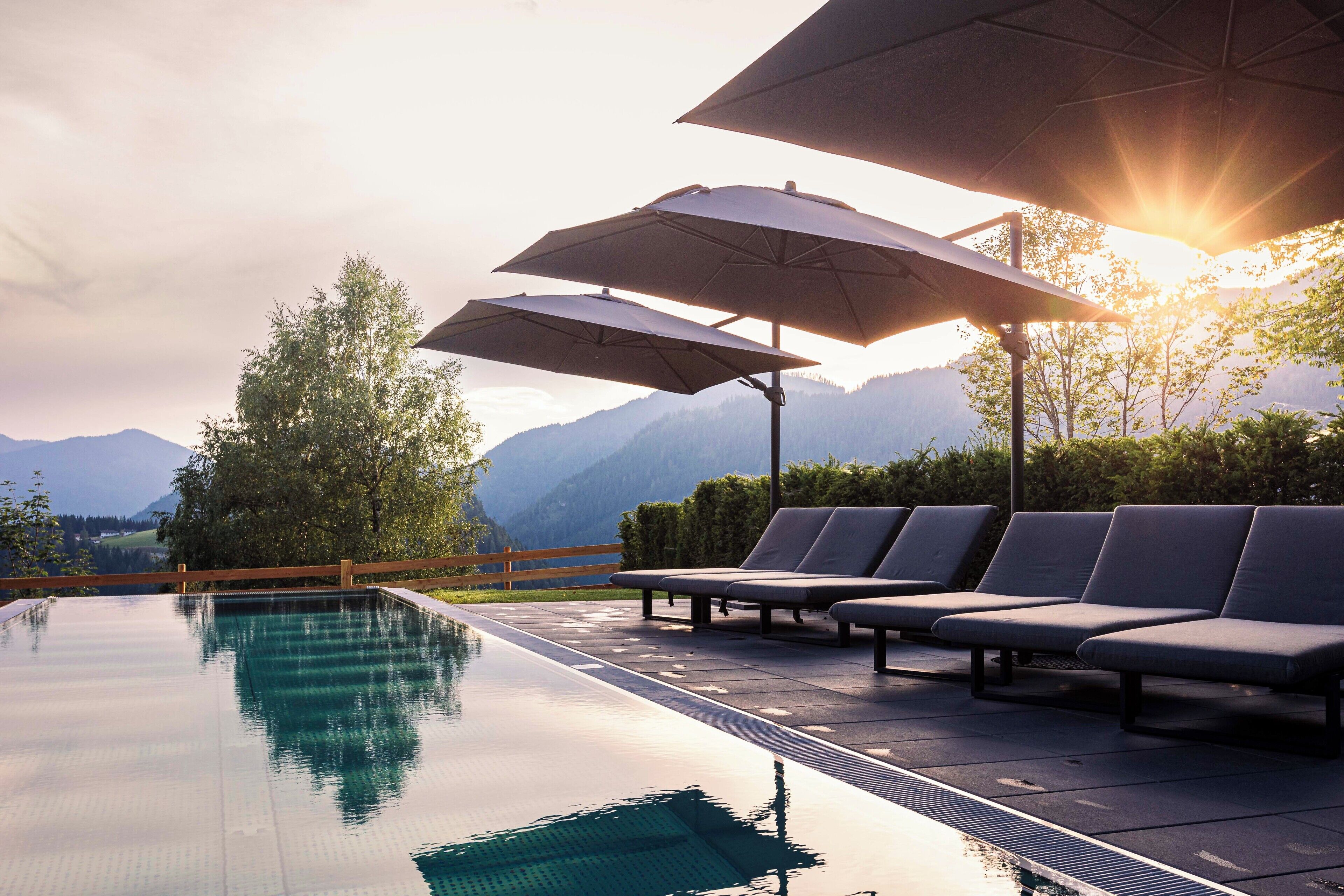 An infinity pool with lounge chairs and umbrellas, overlooking a mountainous landscape.