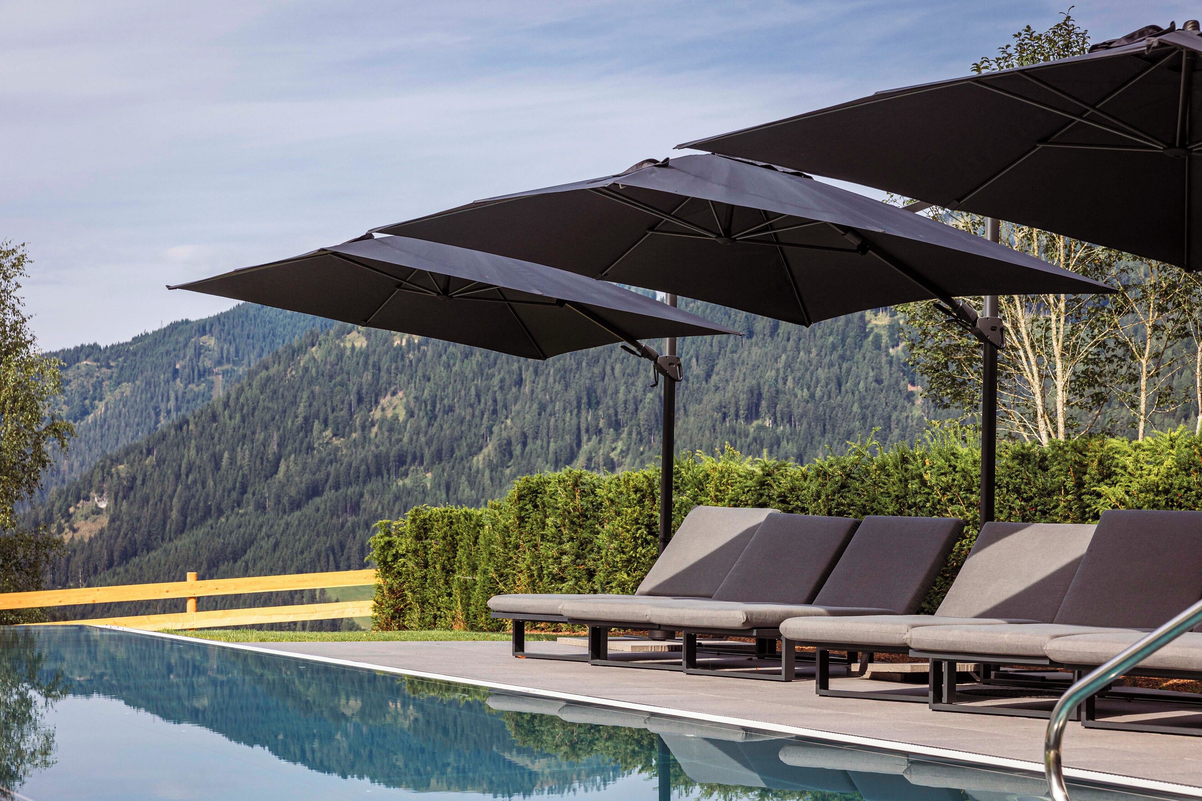 A poolside area with lounge chairs and umbrellas, a wooden deck, and a mountain backdrop.