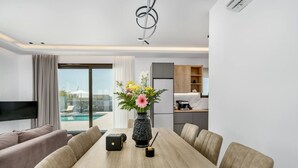 A modern hotel room with a dining area, a TV, a flower vase, and a view of a pool.
