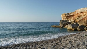 A coastal beach with a rocky cliff and calm sea.
