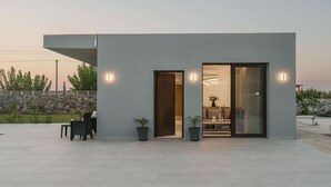 A modern building with a flat roof, a large sliding glass door, and a small outdoor seating area with a table and chairs.