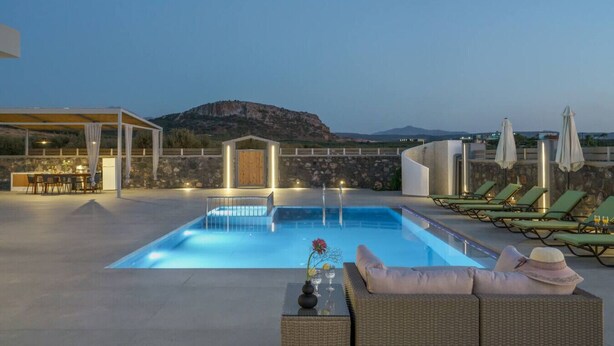 A rooftop pool with lounge chairs, a dining area, and a view of mountains.