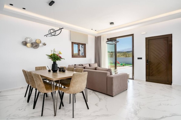 A modern living room with a dining area, a sofa set, and a large window with a view.
