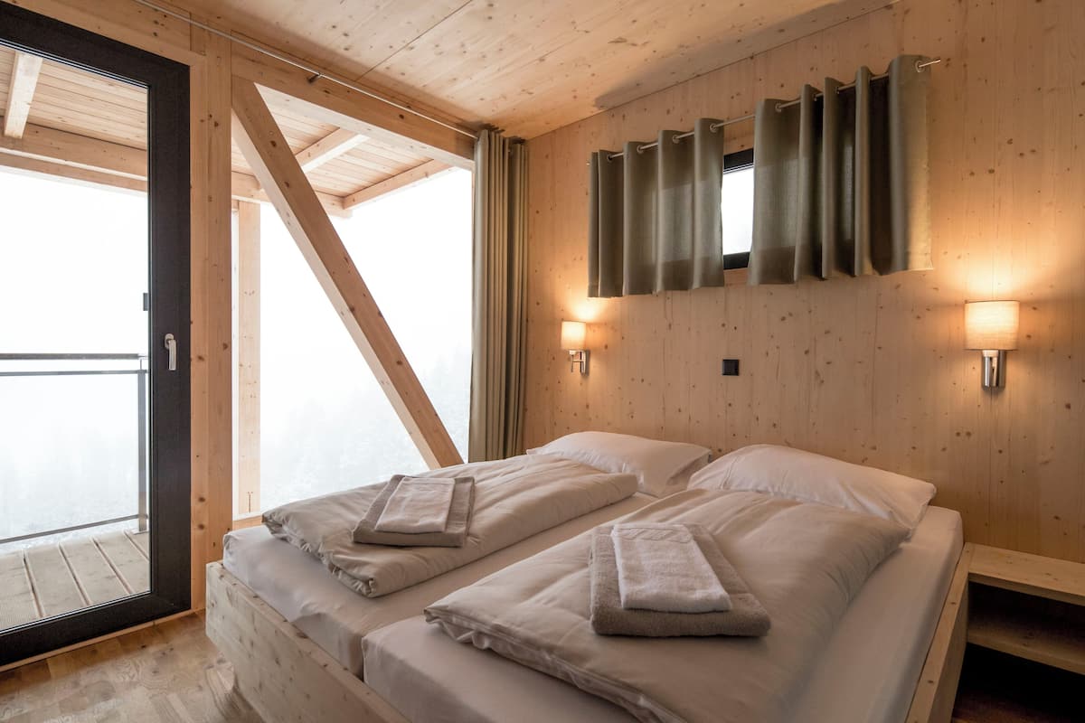 A room with two beds, wooden walls, a large window, and a sliding door.