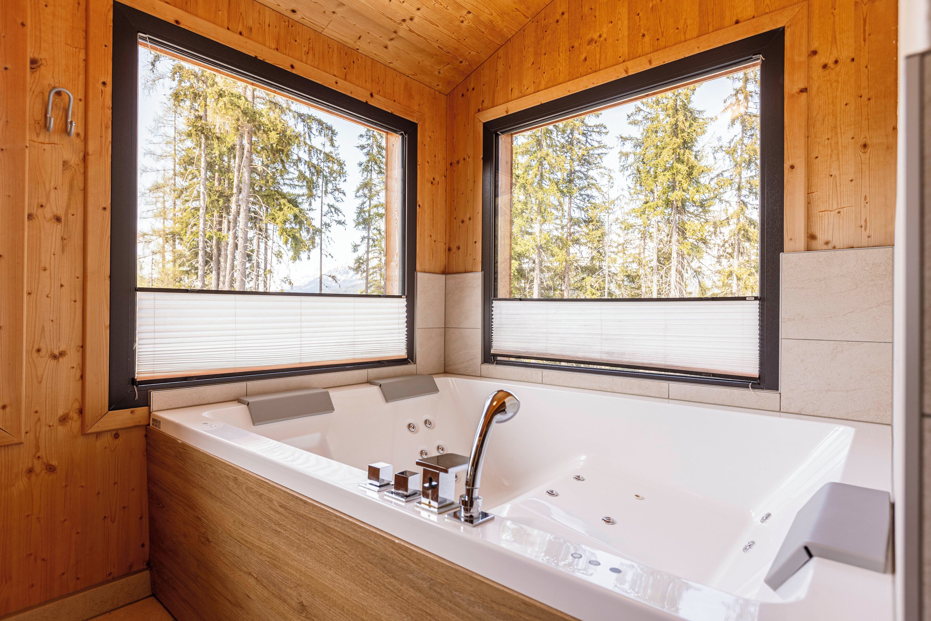 Een moderne badkamer met een groot bad, houten wanden en ramen met uitzicht op een bos.