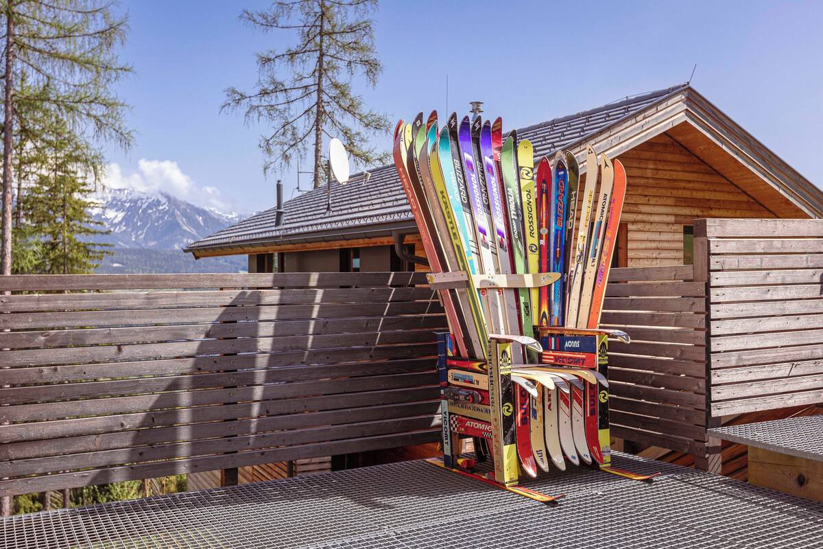 A wooden cabin with a sloped roof, a bench, and a collection of skis leaning against the cabin.