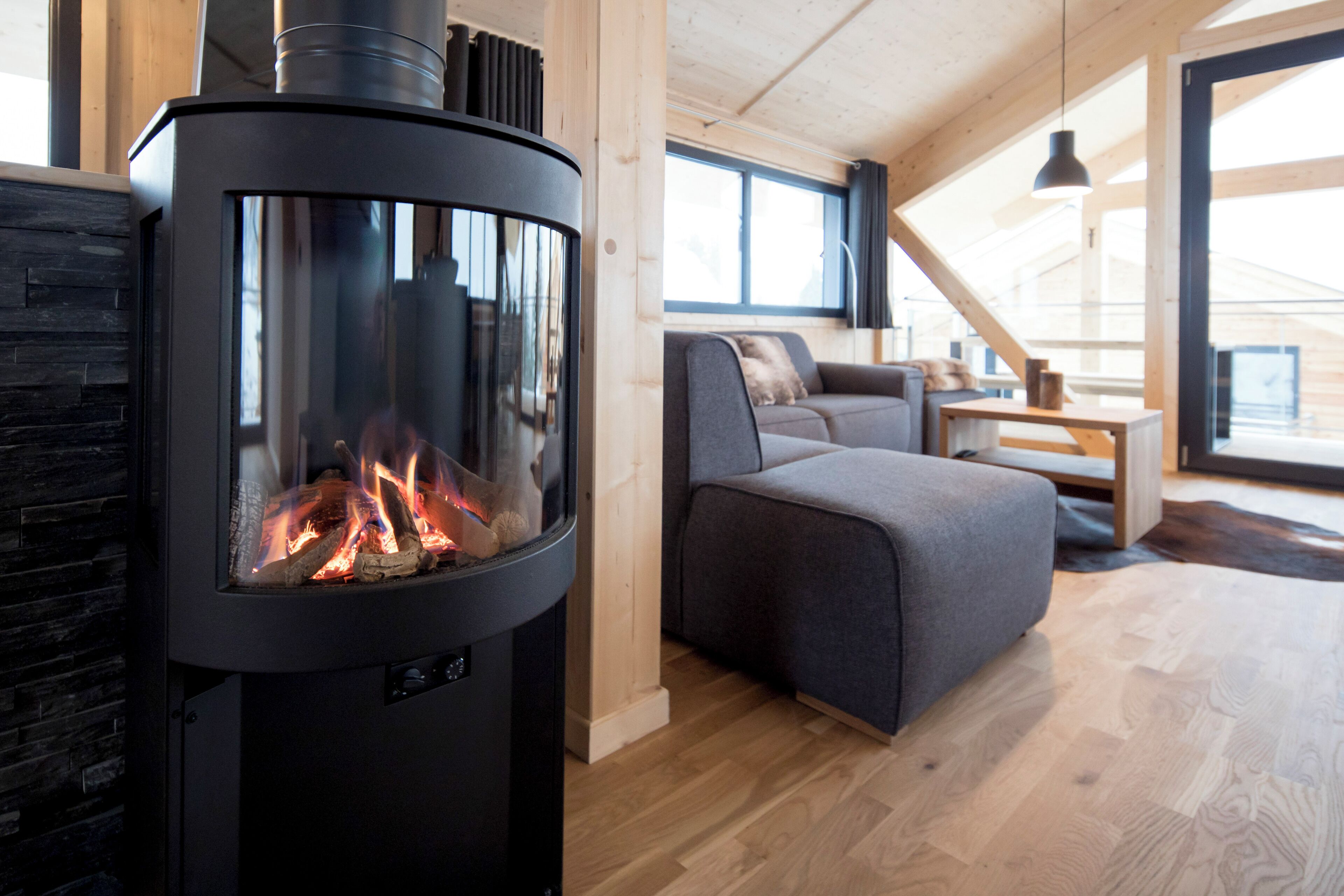 Ein modernes Wohnzimmer mit Kaminofen, grauem Sofa und Holzboden.