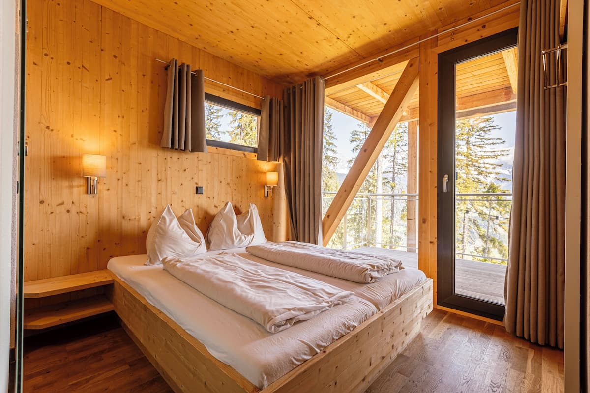 A wooden cabin bedroom with a bed, two bedside lamps, and a window with curtains.