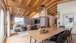 A spacious living area with a wooden ceiling, a large wooden dining table, and a comfortable seating arrangement. - Chalet 149 Westendorf by ALPS RESORTS (Westendorf)