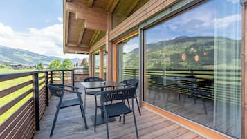 Eine Holzterrasse mit Sitzgelegenheiten im Freien und großen Fenstern, die einen Blick auf eine grüne Landschaft bieten.