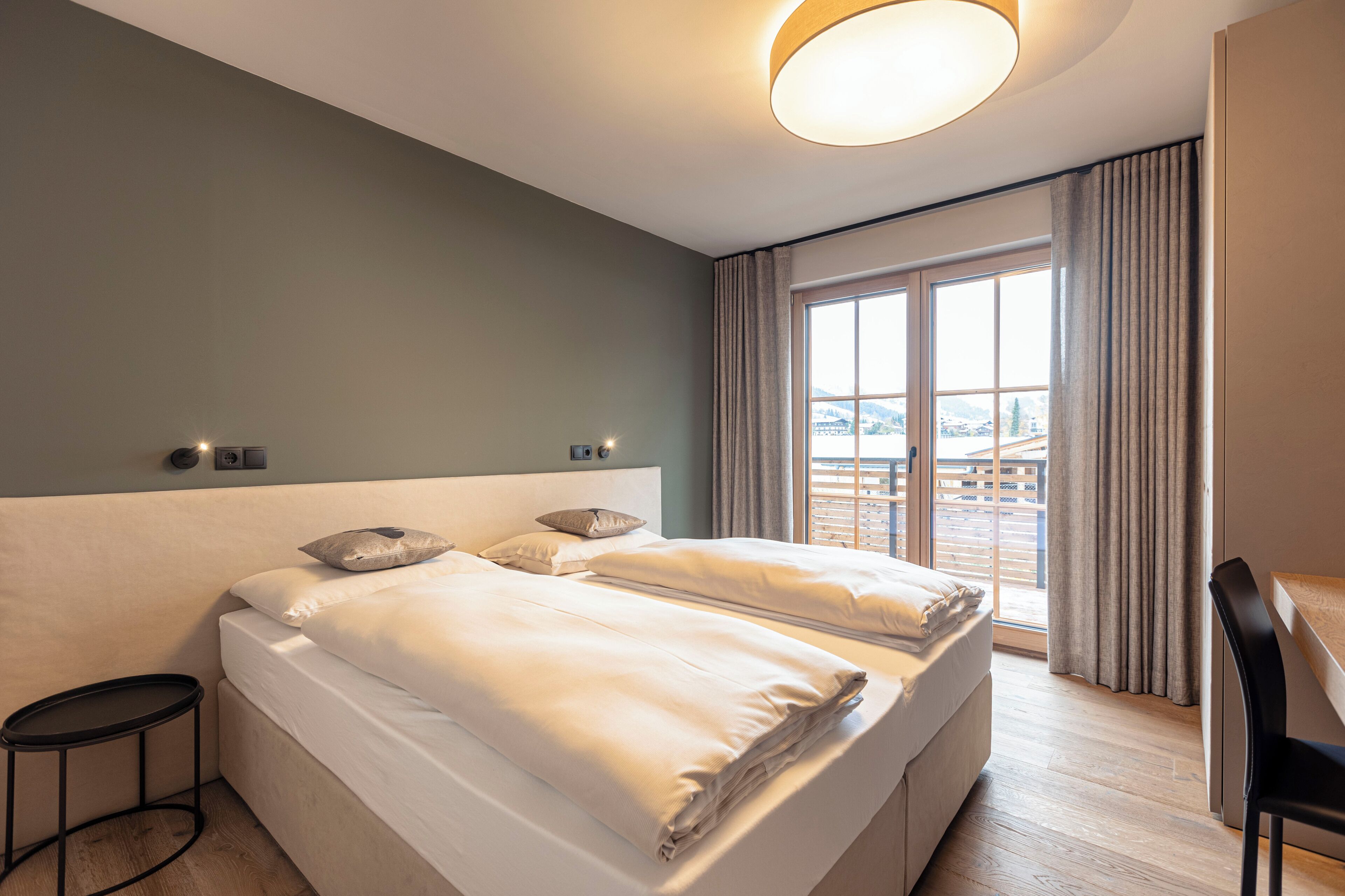 A hotel room with a large bed, a desk, and a view of the city through the window.