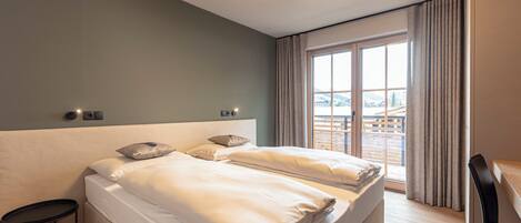 A hotel room with a large bed, a desk, and a view of the city through the window.